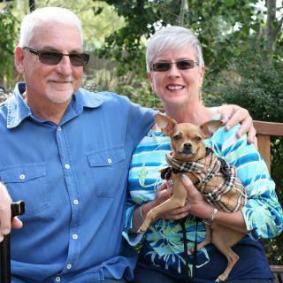 A smiling couple sitting outdoors with their small dog.