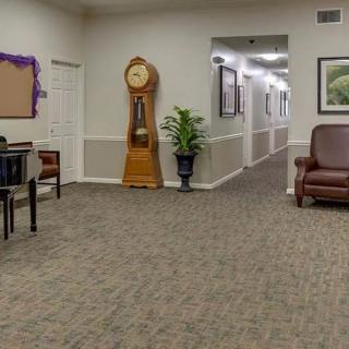 A waiting room with a large clock, seating area, and decorative plants leading to a hallway.