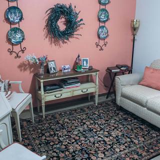 A cozy living room with a decorative wreath and plates on a coral wall, featuring a sofa and a patterned rug.