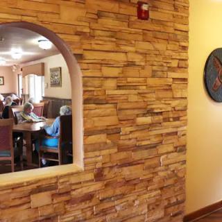 A cozy restaurant interior featuring a brick wall with an archway, revealing a dining area where guests are seated.