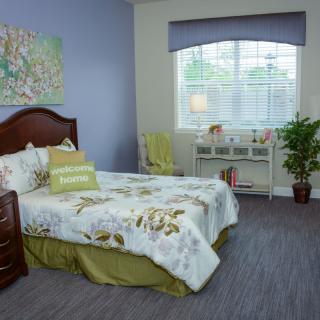 A cozy bedroom with floral bedding, a wooden headboard, and a desk by the window.