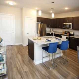 A modern kitchen with an open-concept design featuring a central island with blue bar stools and stainless steel appliances.