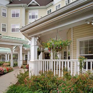 A charming residential building with a spacious porch adorned with hanging plants and surrounded by well-maintained landscaping.