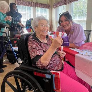 A joyful moment at a community event, where an elderly woman enjoys a treat while being supported by a caregiver.