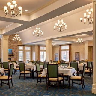 Elegant dining room with upholstered chairs, set tables, and multiple chandeliers.