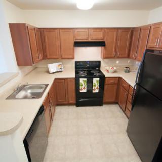 A modern kitchen featuring wooden cabinets, a black oven, refrigerator, and a stainless steel sink.