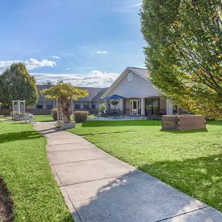 A picturesque front yard with a pathway leading to a house, surrounded by trees and a well-maintained lawn under a clear sky.