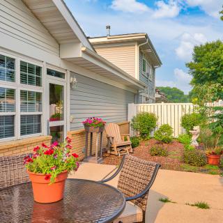 A cozy patio area with outdoor furniture and vibrant flowers, set against a house exterior on a sunny day.