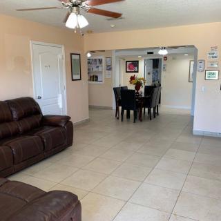 A spacious living room with tiled flooring and a ceiling fan, leading to a dining area.