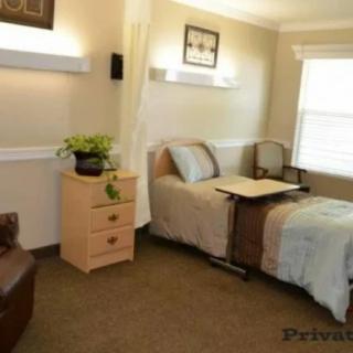 A cozy bedroom with a single bed, dresser, and chair, featuring soft lighting and a window.