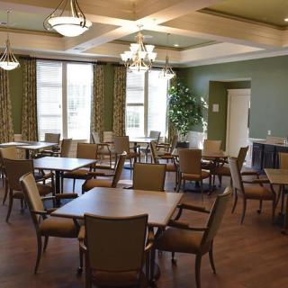 A well-lit dining room with neatly arranged tables and chairs, featuring large windows and elegant chandeliers.