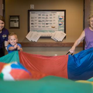 Children and adults play with a colorful parachute indoors, enjoying fun activities.