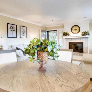 A well-lit living room with a dining area, featuring a round wooden table, chairs, and a fireplace adorned with decorative elements.