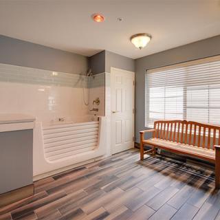A minimalist bathroom with a bathtub, hardwood floor, and a wooden bench by the window.