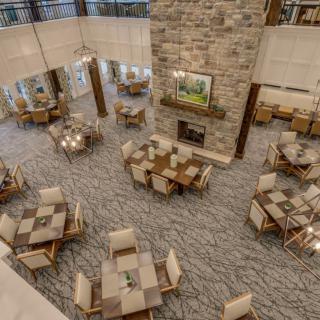 A spacious dining area with multiple wooden tables and chairs, featuring a large stone fireplace.