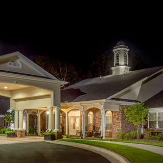 A beautifully lit building entrance at night, showcasing elegant architecture and manicured landscaping.
