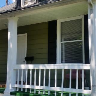 A small porch with a column and railing on the side of a house.