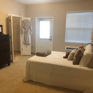 A cozy bedroom with a neatly made bed, dresser, and natural light from the window.
