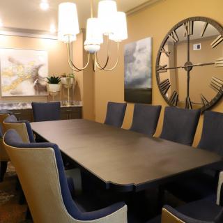 A stylish dining room featuring a large table, elegant chairs, a decorative wall clock, and modern lighting.