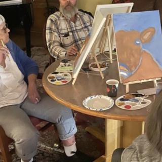 A group of people engaged in a painting session, working on canvases at a table.