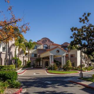A scenic view of a residential building with a welcoming entrance surrounded by lush greenery and trees on a sunny day.