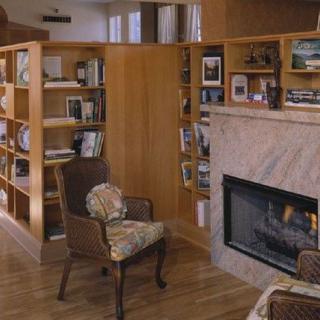 A cozy library interior with wooden bookshelves, a fireplace, and an armchair.