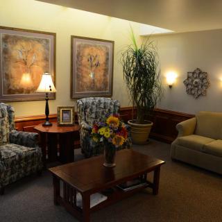 A cozy living room with floral armchairs, a sofa, a wooden coffee table with a vase of flowers, and decorative wall art.
