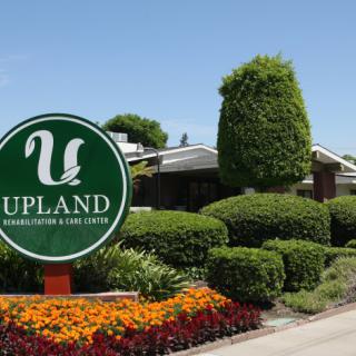 A landscaped entrance with a sign reading 'Upland' in front of a building.