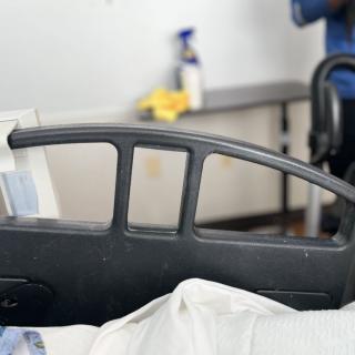 A hospital bed with cleaning supplies in the background.