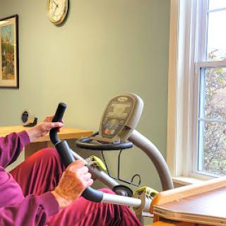 A senior individual exercising on a stationary bike in a well-lit room.