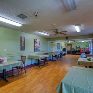 An empty room with green walls, wooden flooring, and tables arranged with chairs.
