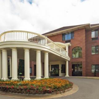 A building with a brick exterior features a grand entrance with columns and well-maintained landscaping.
