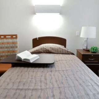 A neatly made bed with a book open on a tray, accompanied by a nightstand and lamp.