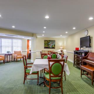 A cozy dining area with tables, chairs, a piano, and a television.
