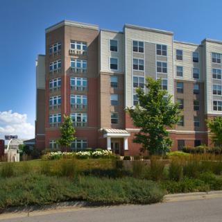 A modern residential apartment building with landscaped surroundings under a clear blue sky.