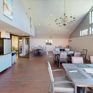 A modern dining area with tables, chairs, and chandeliers, featuring ample natural light from large windows.