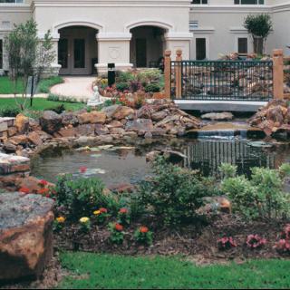 A beautifully landscaped garden with a pond and rocks in front of a building.