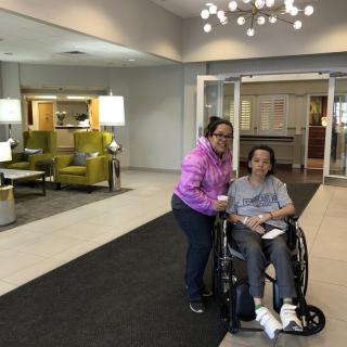 A person in a wheelchair accompanied by another individual in a lobby setting.
