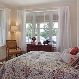 A cozy bedroom with a large window, floral bedding, and classic furnishings.