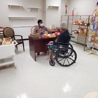 A caregiver engages with an elderly person in a wheelchair at a desk, fostering communication and support in a welcoming indoor space.