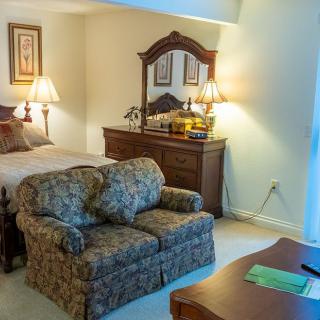 A cozy bedroom featuring a comfortable bed, patterned sofa, wooden dresser with lamps, and elegant decor.