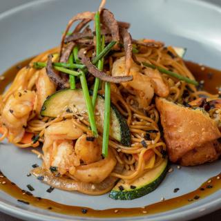 A delicious plate of noodles topped with shrimp, tofu, and vegetables, garnished with herbs.