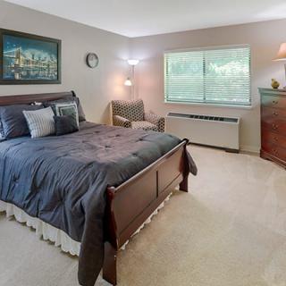 A cozy bedroom with a large bed, armchair, and dresser under natural light.