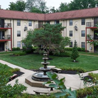 A view of an apartment complex with a landscaped courtyard featuring a central fountain and lush greenery.