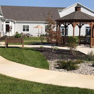 A beautifully landscaped garden area with a gazebo, benches, and a winding pathway in front of a building.