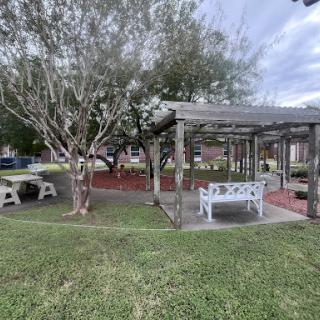 A tranquil outdoor space featuring a seating area under a pergola surrounded by lush greenery.