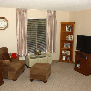 A cozy living room with an armchair, ottoman, bookshelf, and television.