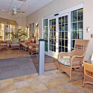 A cozy lobby with wicker furniture and glass doors, featuring a comfortable seating area and indoor plants.