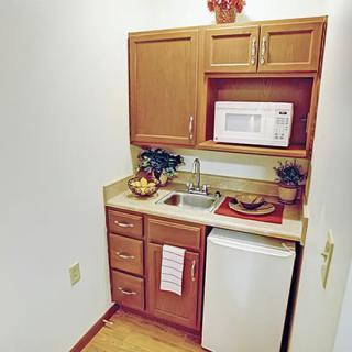 A compact kitchenette featuring a microwave, mini fridge, sink, and wooden cabinetry.