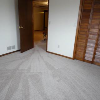 An empty room with freshly vacuumed carpet, an open door, and a wooden closet.